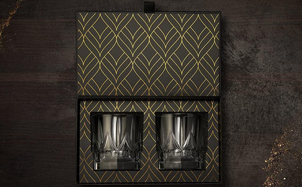 Two glass tumblers in a decorative black and gold box on a dark wooden surface.