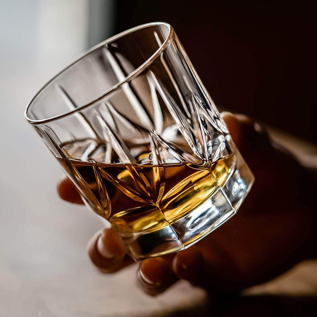 Hand holding a crystal glass filled with whiskey against a neutral background