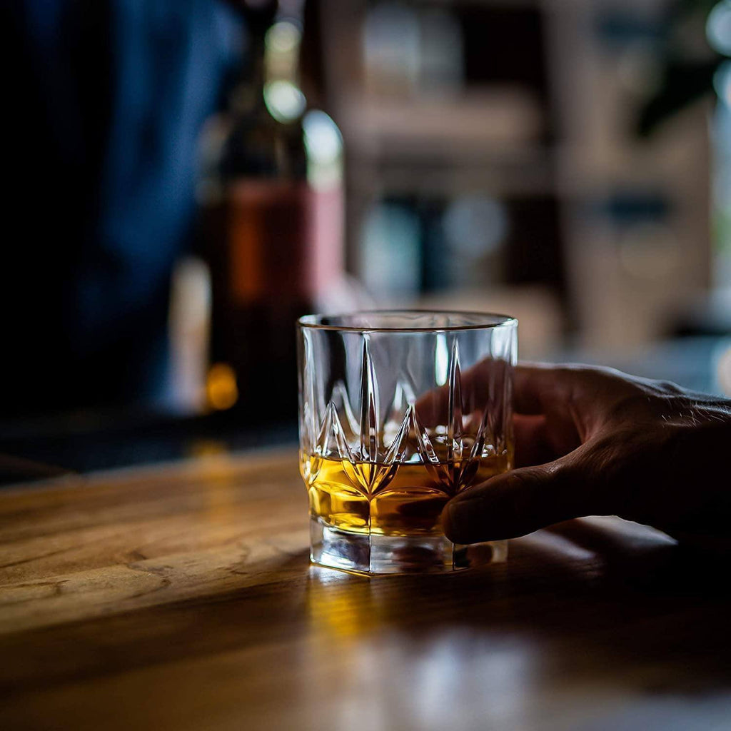 Hand holding a glass of whiskey on a wooden surface with blurred background